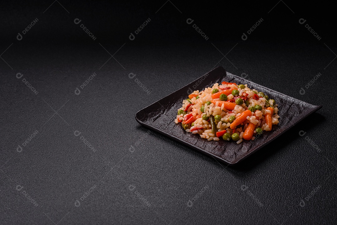 Delicioso arroz cozido com legumes cenouras, ervilhas e pimentões com sal e especiarias sobre um fundo escuro de concreto