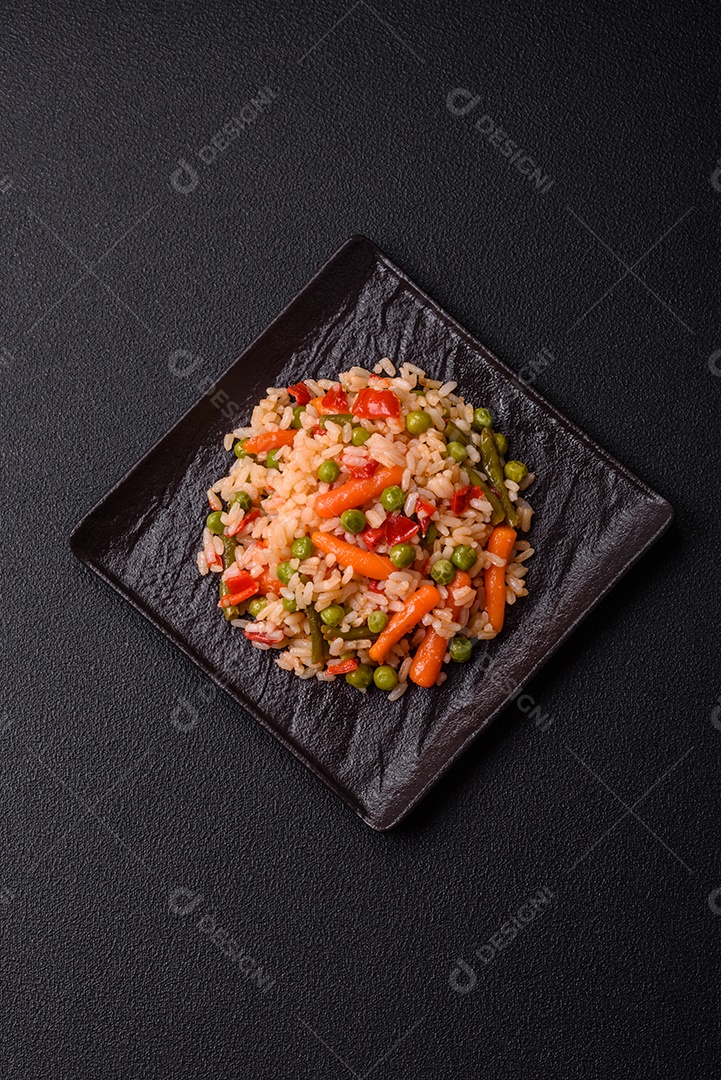 Delicioso arroz cozido com legumes cenouras, ervilhas e pimentões com sal e especiarias sobre um fundo escuro de concreto