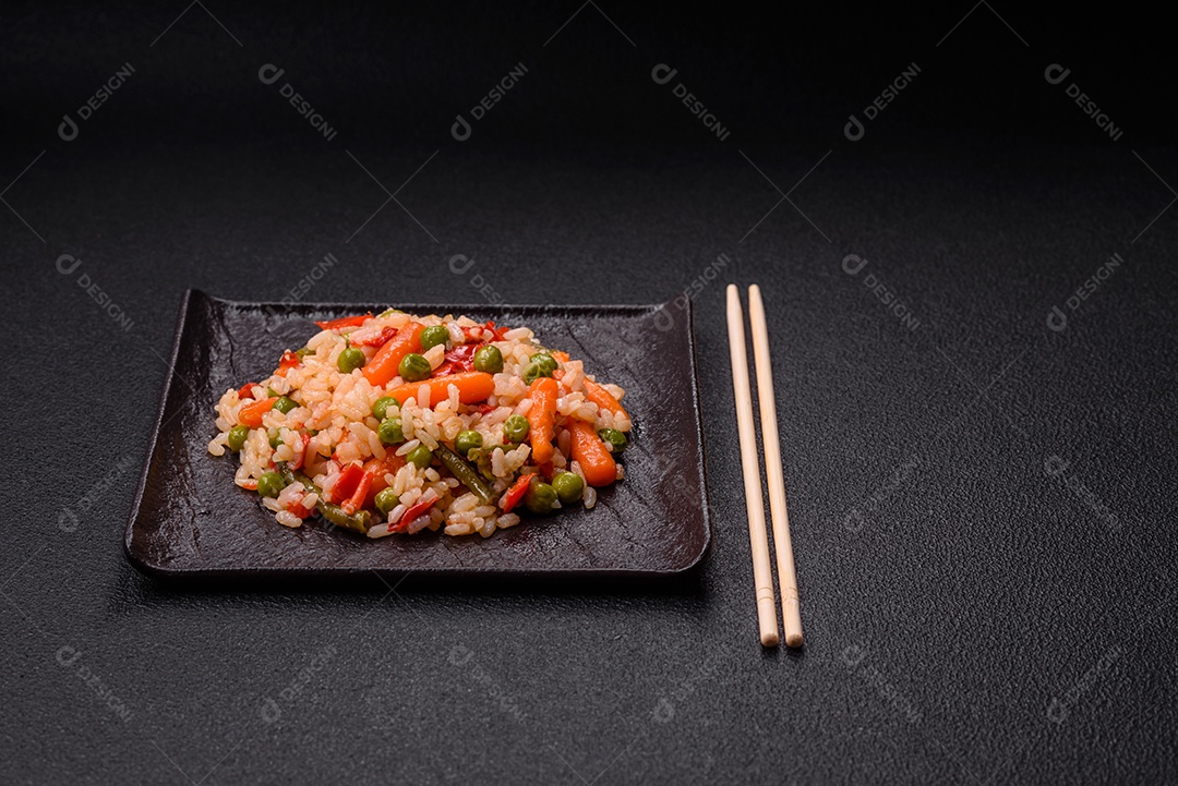 Delicioso arroz cozido com legumes cenouras, ervilhas e pimentões com sal e especiarias sobre um fundo escuro de concreto