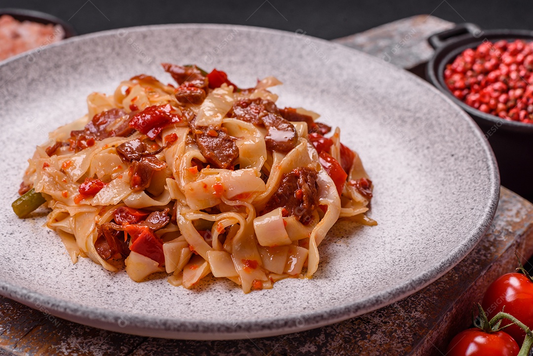 Delicioso prato de udon asiático com legumes, carne, sal e especiarias numa placa cerâmica sobre um fundo escuro de concreto