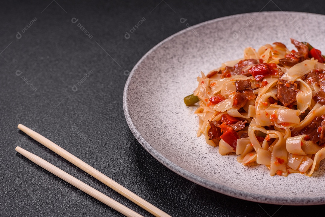 Delicioso prato de udon asiático com legumes, carne, sal e especiarias numa placa cerâmica sobre um fundo escuro de concreto