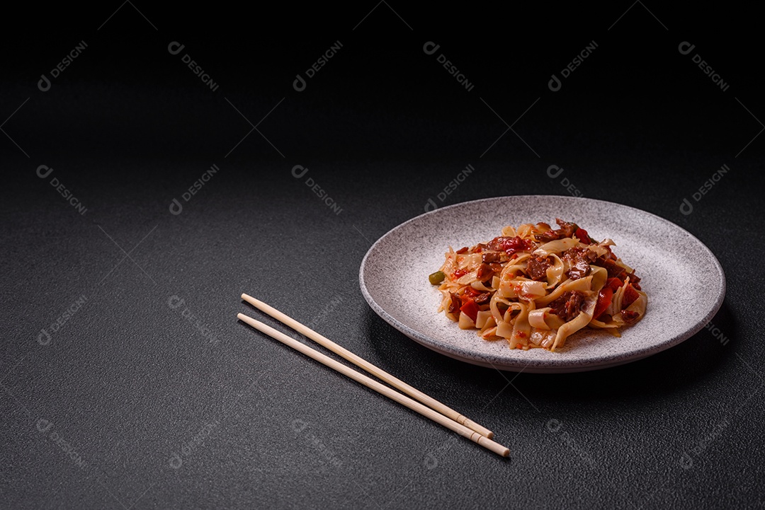 Delicioso prato de udon asiático com legumes, carne, sal e especiarias numa placa cerâmica sobre um fundo escuro de concreto