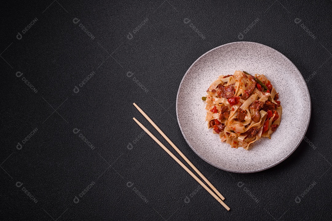 Delicioso prato de udon asiático com legumes, carne, sal e especiarias numa placa cerâmica sobre um fundo escuro de concreto