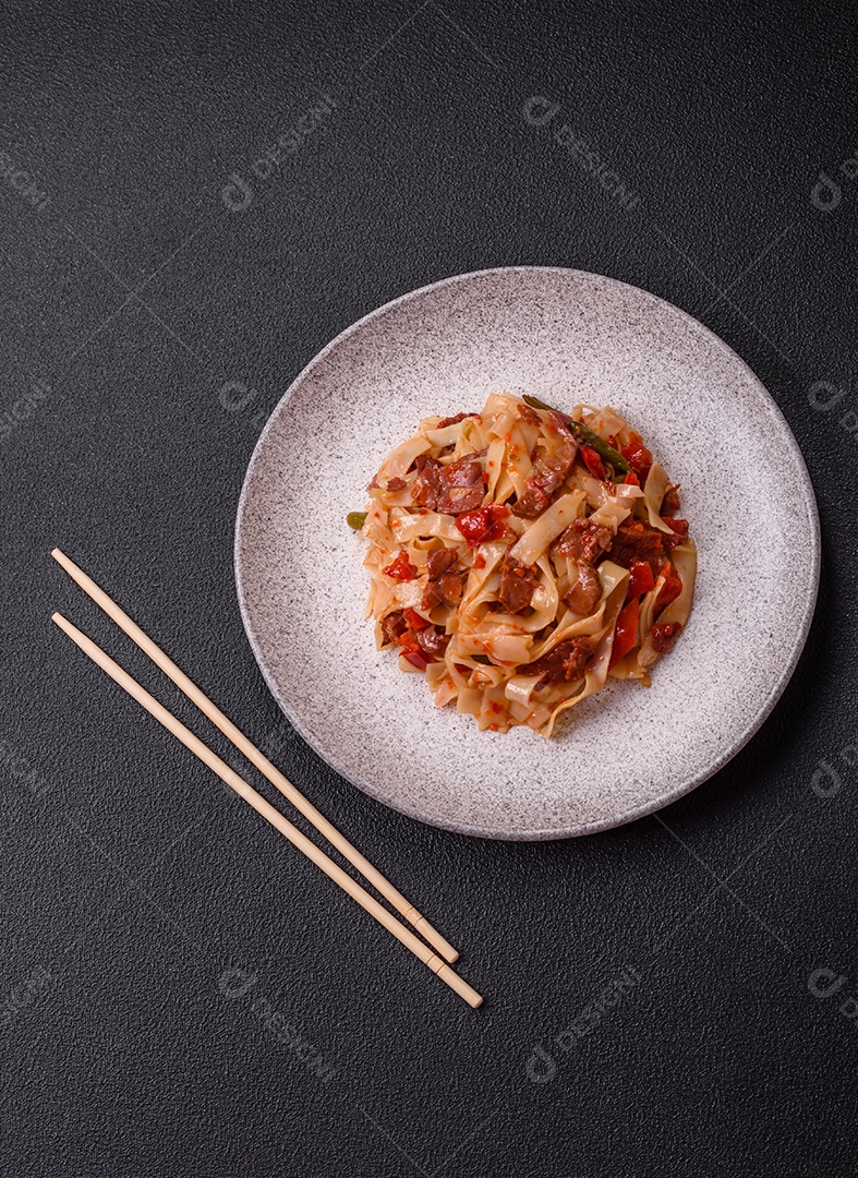 Delicioso prato de udon asiático com legumes, carne, sal e especiarias numa placa cerâmica sobre um fundo escuro de concreto
