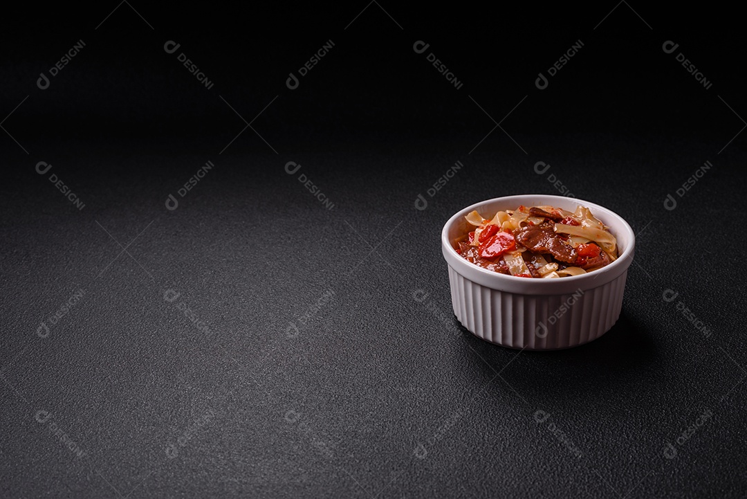 Delicioso prato de udon asiático com legumes, carne, sal e especiarias numa placa cerâmica sobre um fundo escuro de concreto