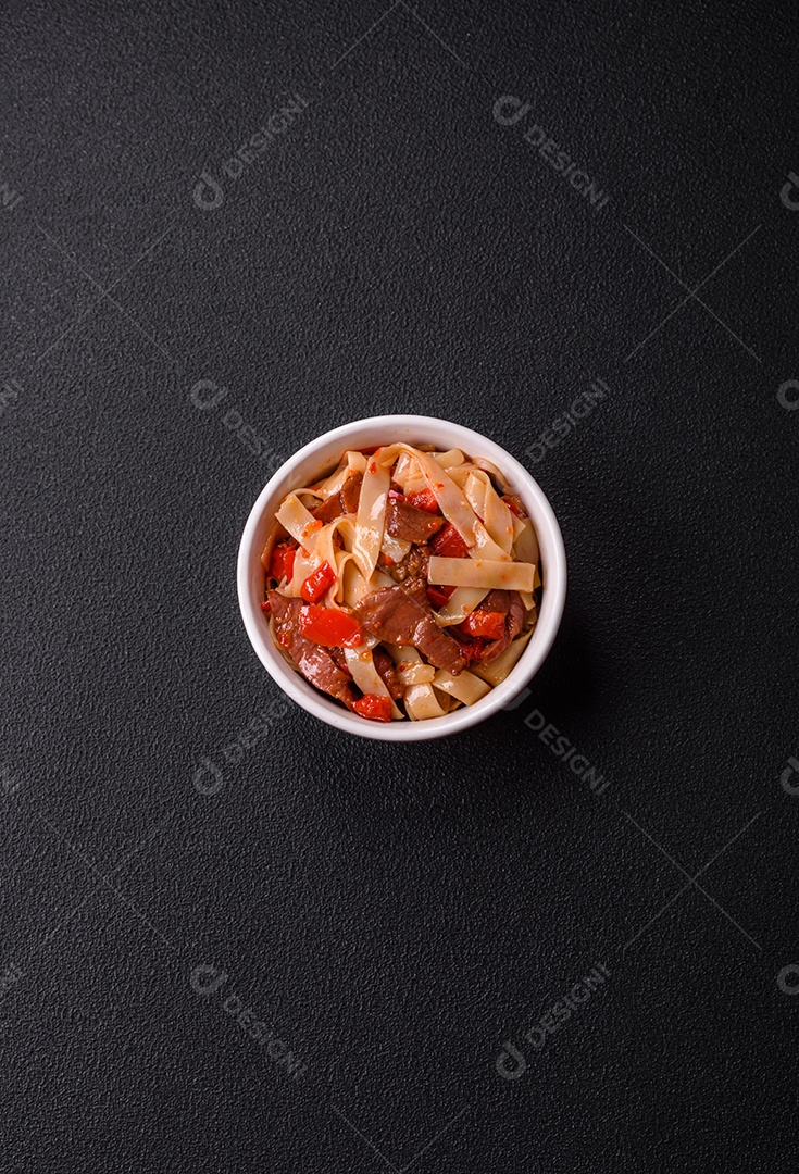 Delicioso prato de udon asiático com legumes, carne, sal e especiarias numa placa cerâmica sobre um fundo escuro de concreto