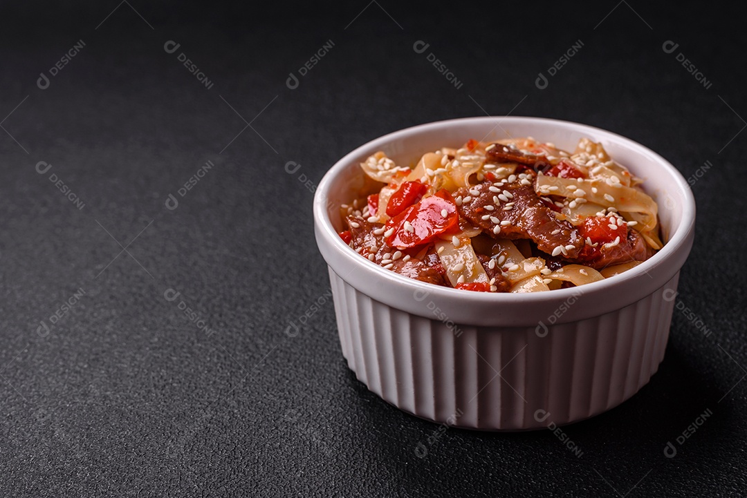 Delicioso prato de udon asiático com legumes, carne, sal e especiarias numa placa cerâmica sobre um fundo escuro de concreto
