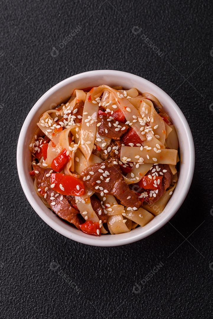 Delicioso prato de udon asiático com legumes, carne, sal e especiarias numa placa cerâmica sobre um fundo escuro de concreto