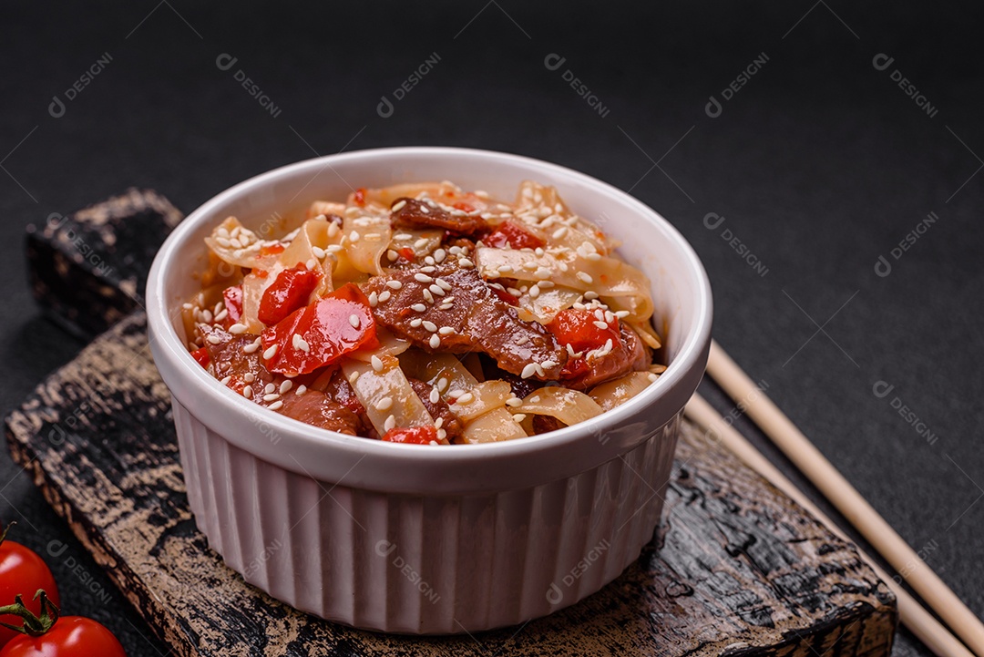 Delicioso prato de udon asiático com legumes, carne, sal e especiarias numa placa cerâmica sobre um fundo escuro de concreto