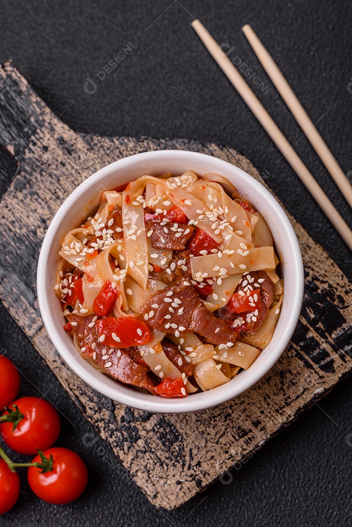 Delicioso prato de udon asiático com legumes, carne, sal e especiarias numa placa cerâmica sobre um fundo escuro de concreto