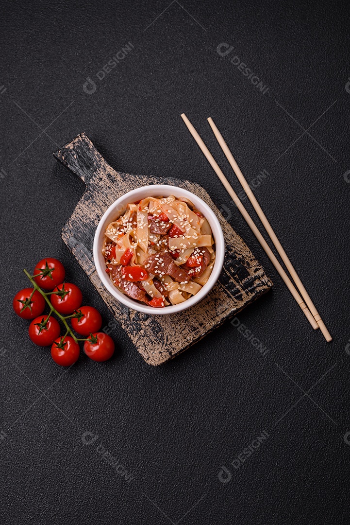 Delicioso prato de udon asiático com legumes, carne, sal e especiarias numa placa cerâmica sobre um fundo escuro de concreto