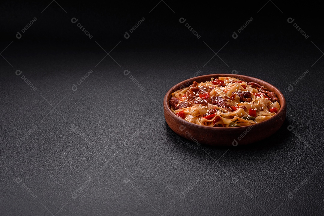 Delicioso prato de udon asiático com legumes, carne, sal e especiarias numa placa cerâmica sobre um fundo escuro de concreto