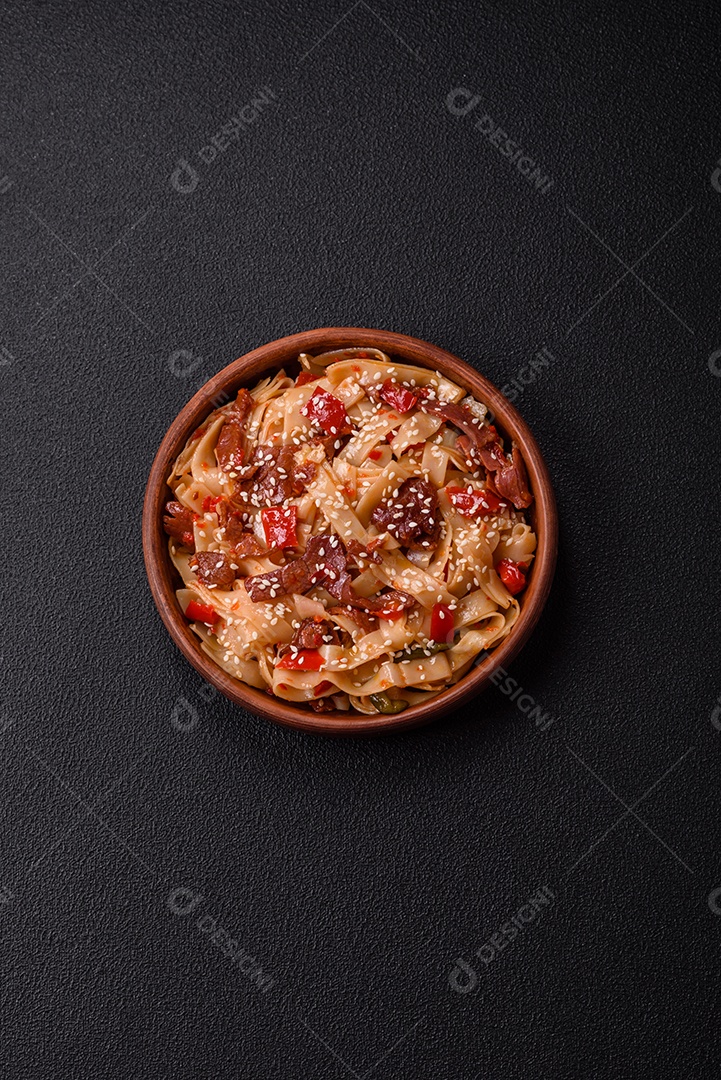 Delicioso prato de udon asiático com legumes, carne, sal e especiarias numa placa cerâmica sobre um fundo escuro de concreto