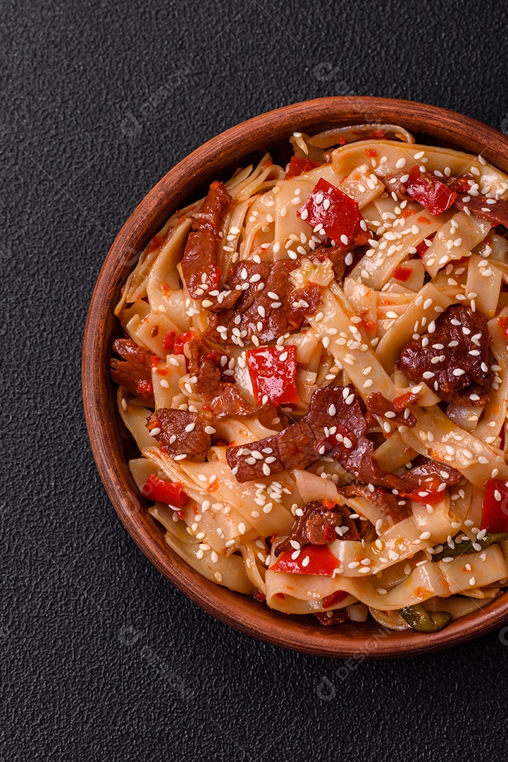 Delicioso prato de udon asiático com legumes, carne, sal e especiarias numa placa cerâmica sobre um fundo escuro de concreto
