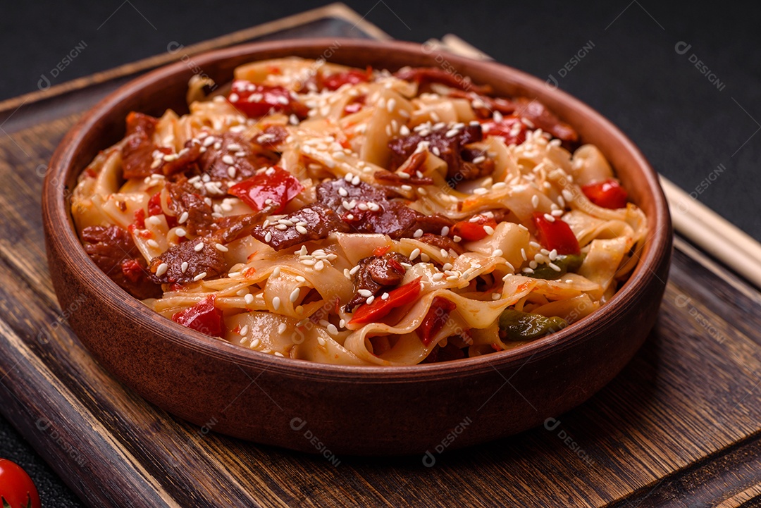 Delicioso prato de udon asiático com legumes, carne, sal e especiarias numa placa cerâmica sobre um fundo escuro de concreto