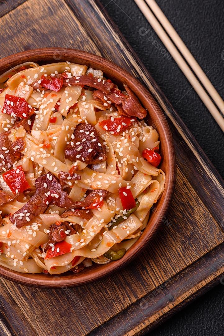 Delicioso prato de udon asiático com legumes, carne, sal e especiarias numa placa cerâmica sobre um fundo escuro de concreto