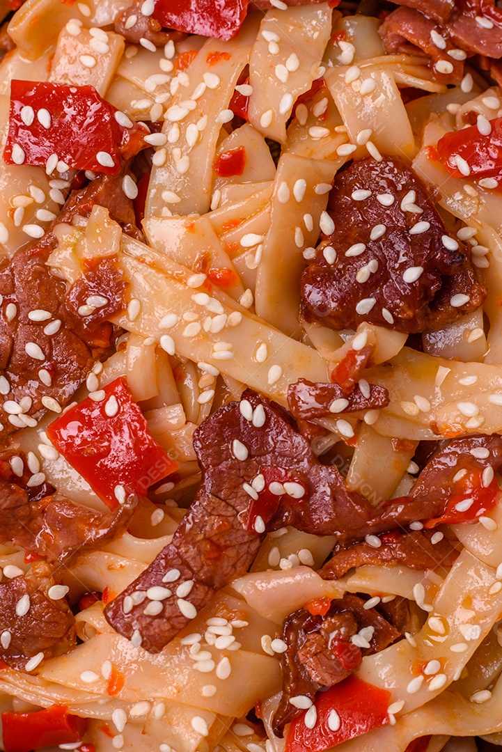 Delicioso prato de udon asiático com legumes, carne, sal e especiarias numa placa cerâmica sobre um fundo escuro de concreto