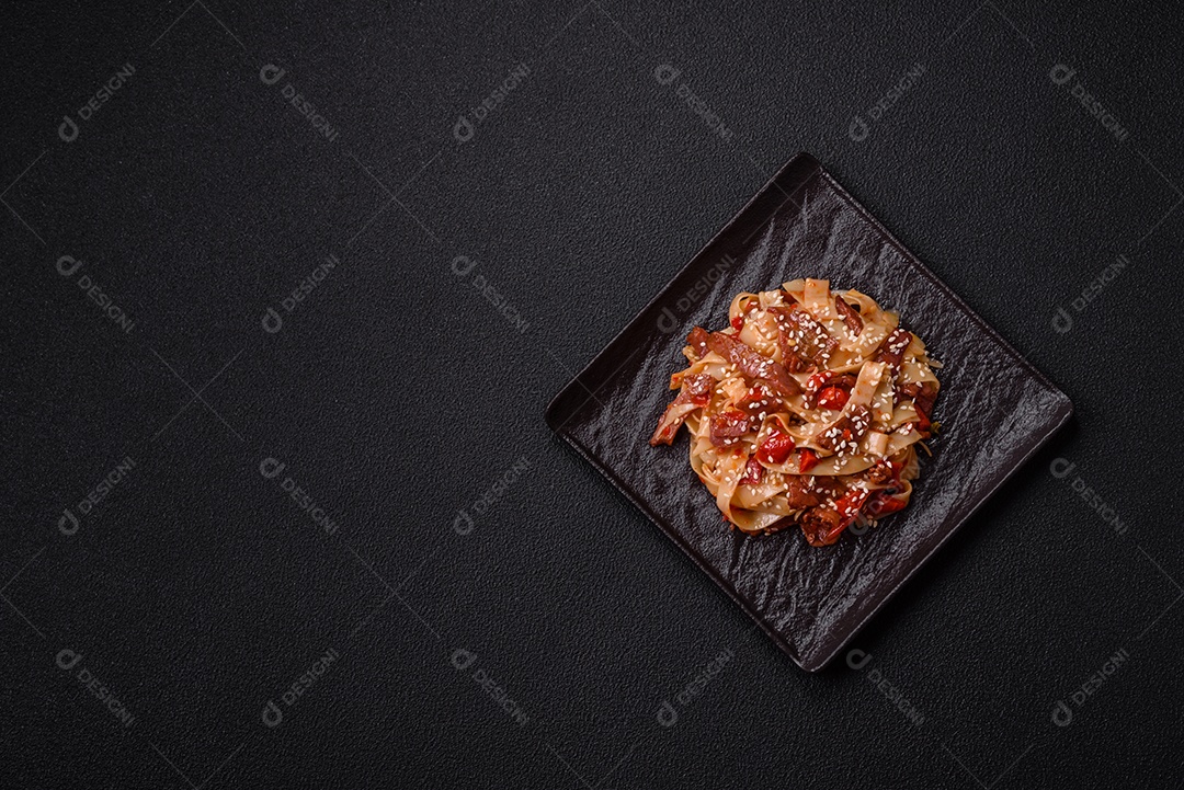 Delicioso prato de udon asiático com legumes, carne, sal e especiarias numa placa cerâmica sobre um fundo escuro de concreto