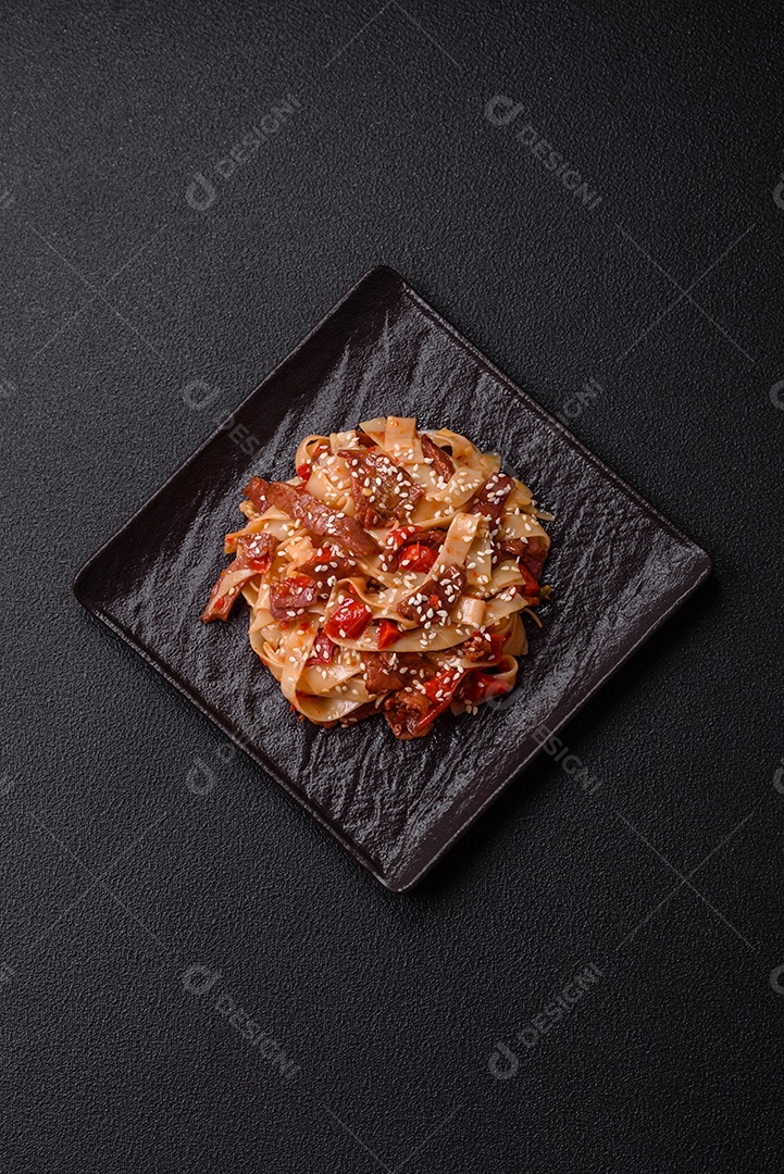 Delicioso prato de udon asiático com legumes, carne, sal e especiarias numa placa cerâmica sobre um fundo escuro de concreto