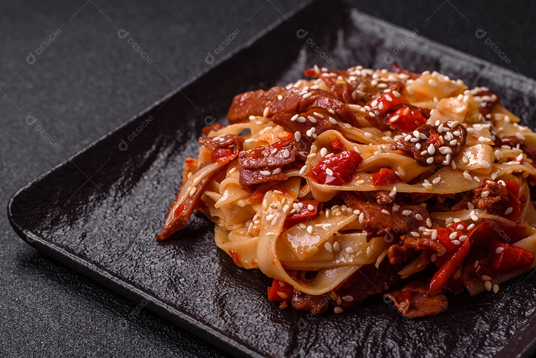 Delicioso prato de udon asiático com legumes, carne, sal e especiarias numa placa cerâmica sobre um fundo escuro de concreto