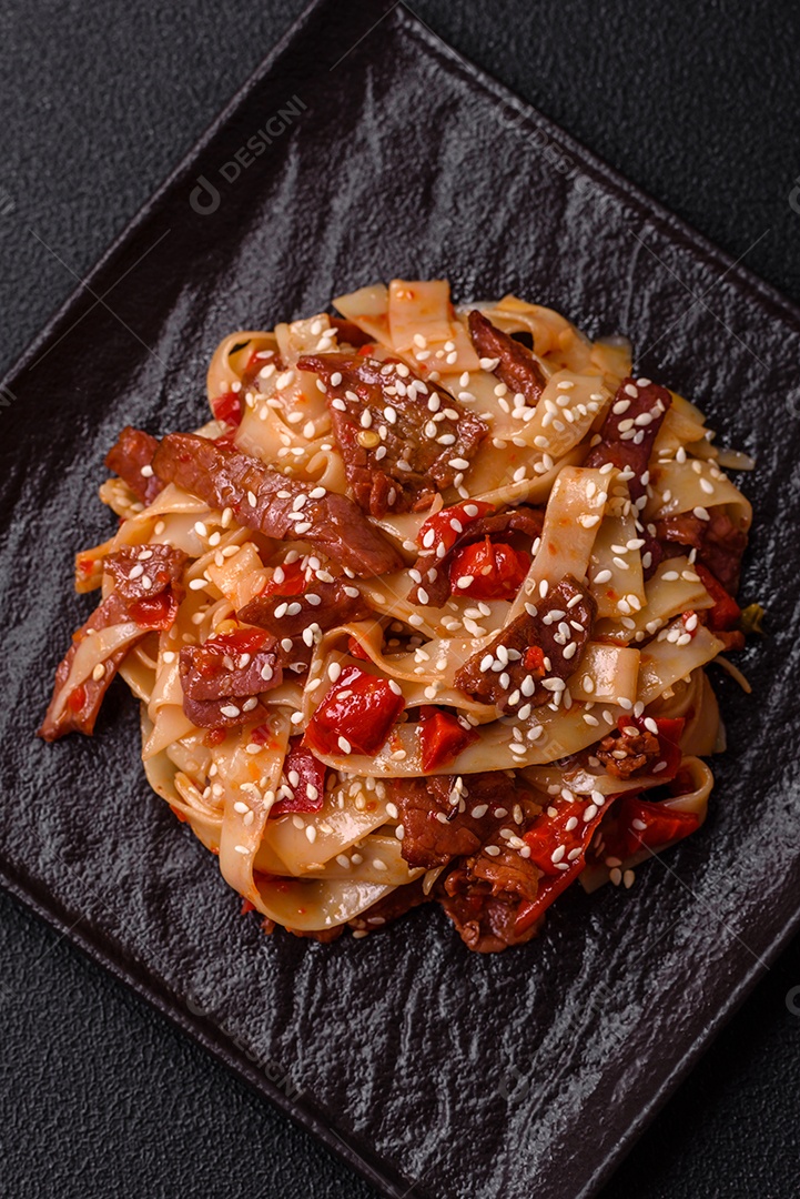 Delicioso prato de udon asiático com legumes, carne, sal e especiarias numa placa cerâmica sobre um fundo escuro de concreto