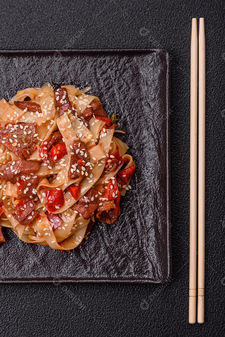 Delicioso prato de udon asiático com legumes, carne, sal e especiarias numa placa cerâmica sobre um fundo escuro de concreto