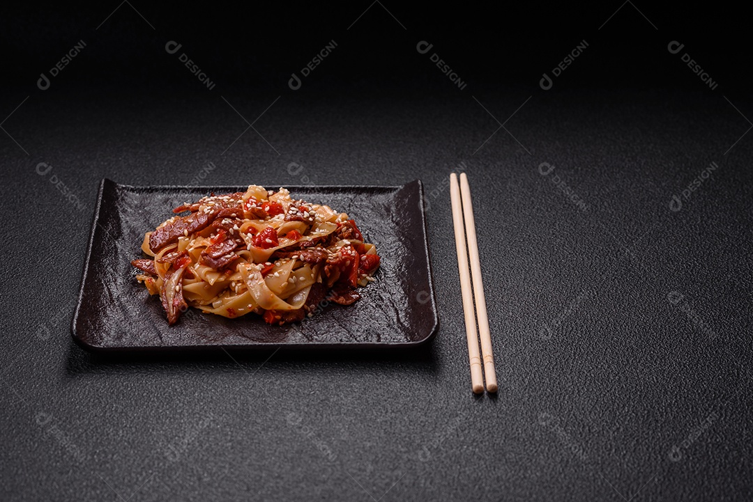 Delicioso prato de udon asiático com legumes, carne, sal e especiarias numa placa cerâmica sobre um fundo escuro de concreto