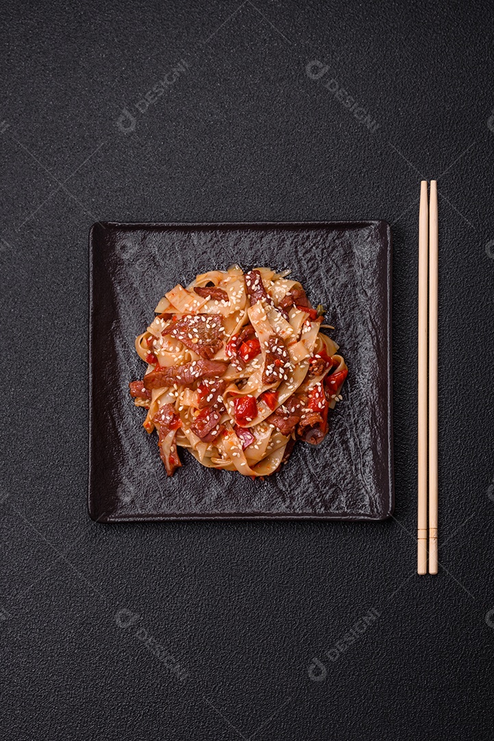Delicioso prato de udon asiático com legumes, carne, sal e especiarias numa placa cerâmica sobre um fundo escuro de concreto