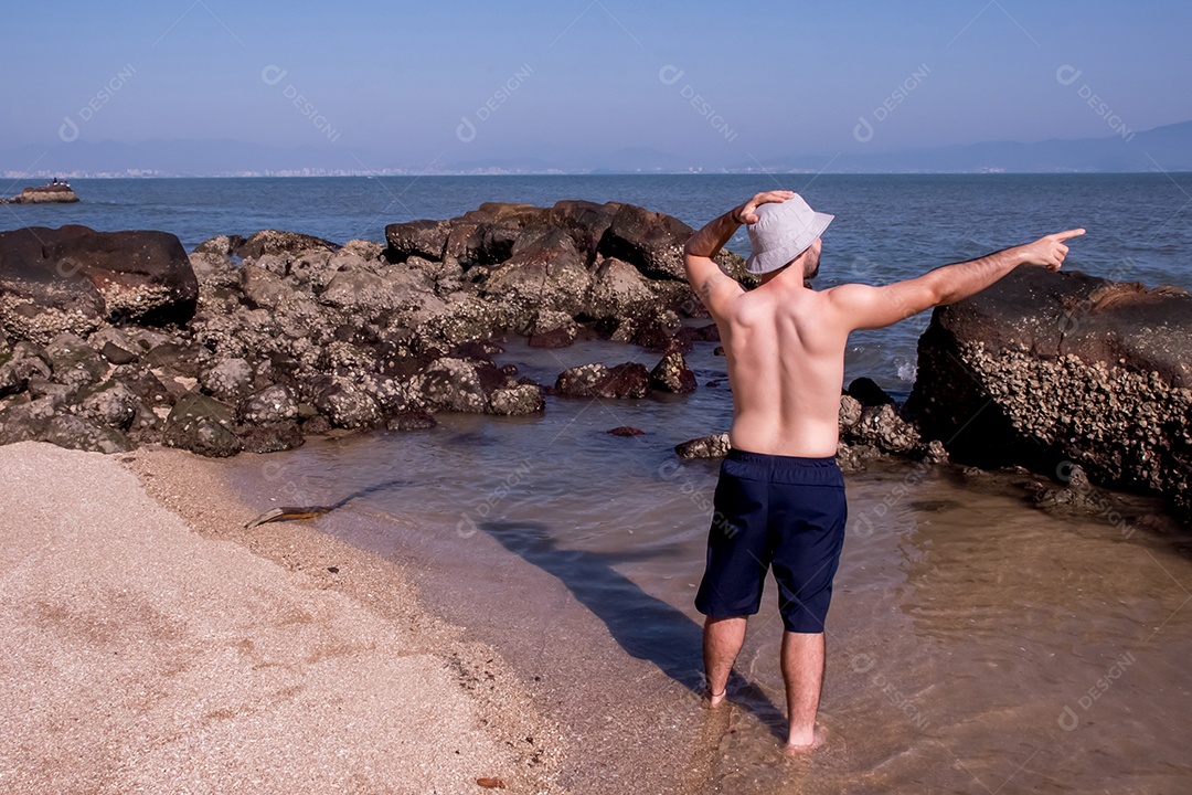 Homem sem camisa na praia apontando para o mar