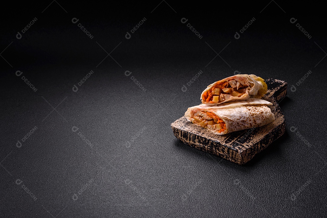 Delicioso rolo suculento ou shawarma com frango, tomate, salada e molho sobre um fundo escuro de concreto
