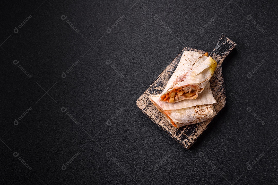 Delicioso rolo suculento ou shawarma com frango, tomate, salada e molho sobre um fundo escuro de concreto