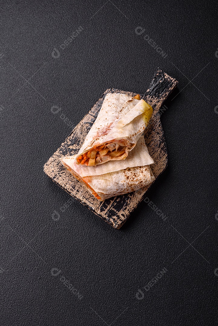 Delicioso rolo suculento ou shawarma com frango, tomate, salada e molho sobre um fundo escuro de concreto