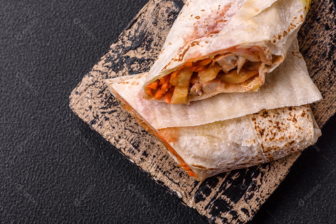 Delicioso rolo suculento ou shawarma com frango, tomate, salada e molho sobre um fundo escuro de concreto