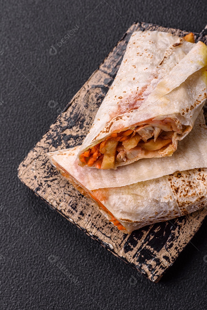 Delicioso rolo suculento ou shawarma com frango, tomate, salada e molho sobre um fundo escuro de concreto