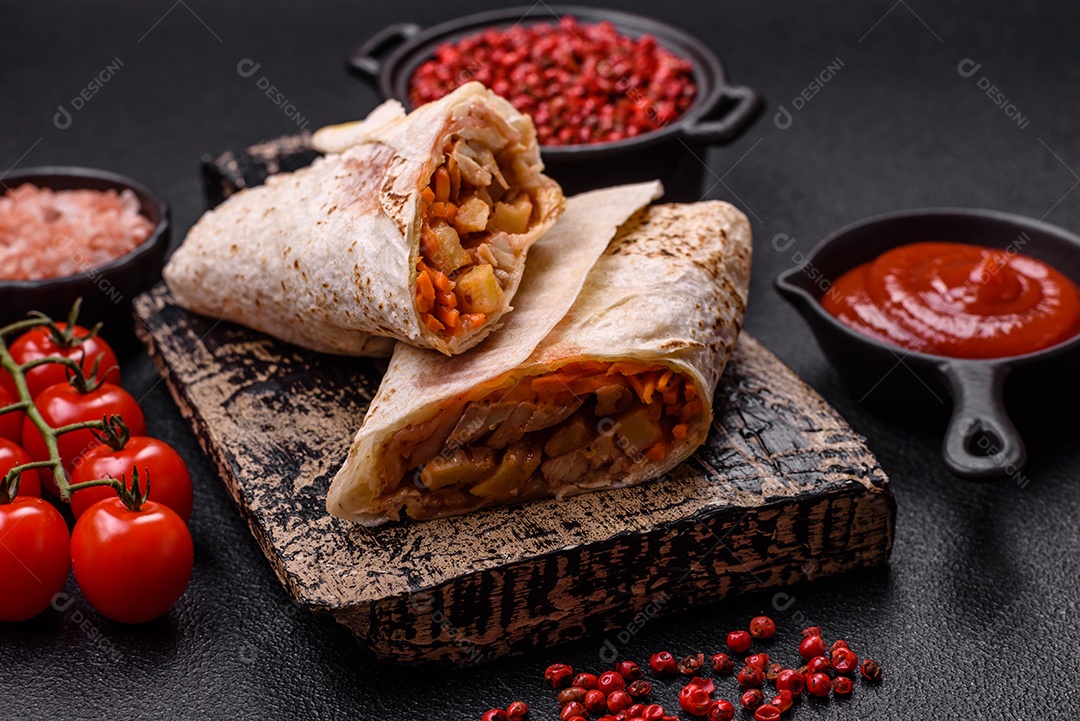 Delicioso rolo suculento ou shawarma com frango, tomate, salada e molho sobre um fundo escuro de concreto
