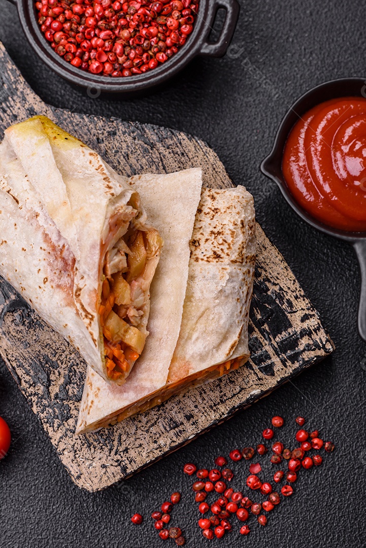 Delicioso rolo suculento ou shawarma com frango, tomate, salada e molho sobre um fundo escuro de concreto