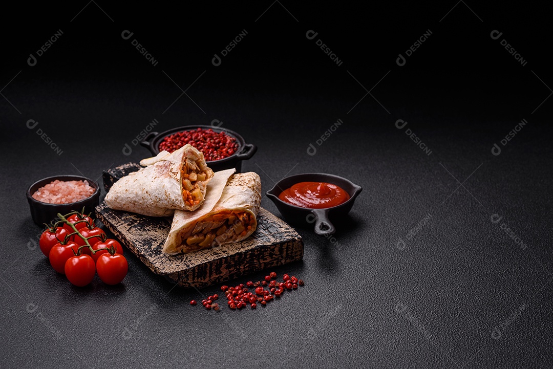 Delicioso rolo suculento ou shawarma com frango, tomate, salada e molho sobre um fundo escuro de concreto