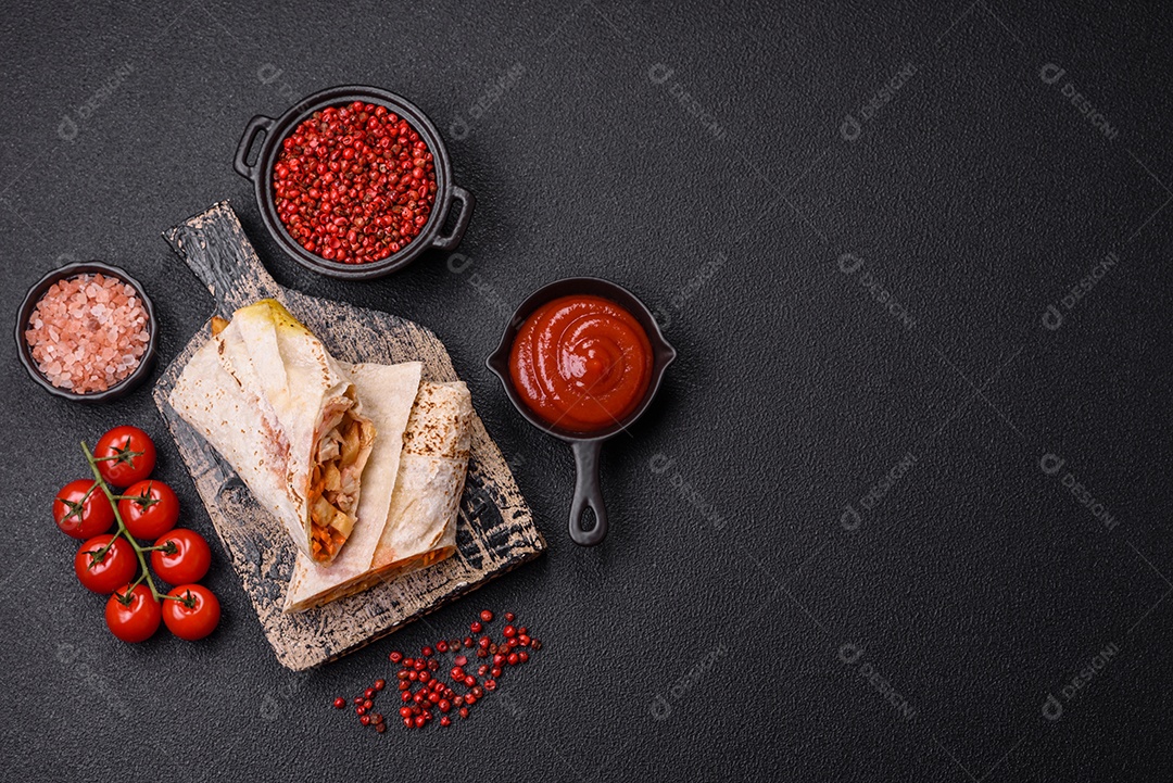 Delicious juicy roll or shawarma with chicken, tomato, salad and sauce on a dark concrete background