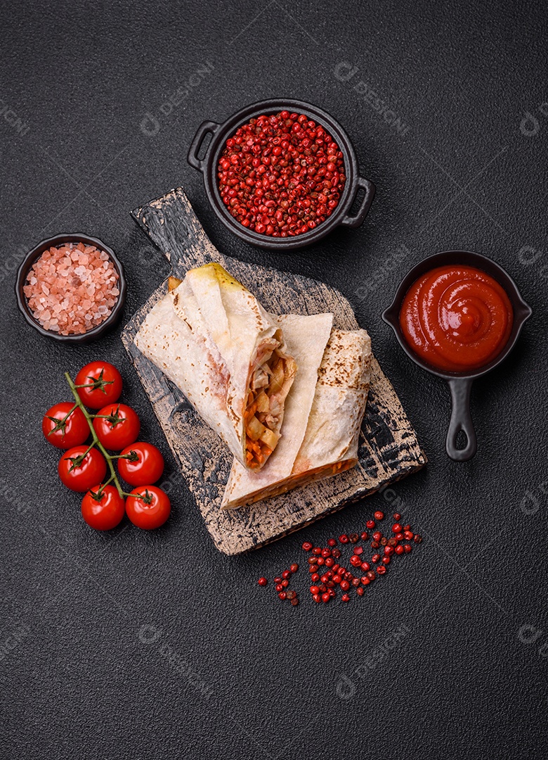 Delicioso rolo suculento ou shawarma com frango, tomate, salada e molho sobre um fundo escuro de concreto