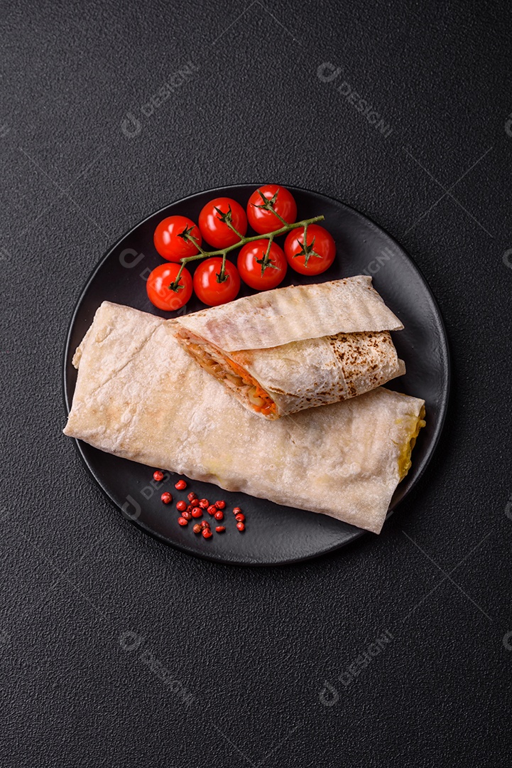 Delicioso rolo suculento ou shawarma com frango, tomate, salada e molho sobre um fundo escuro de concreto