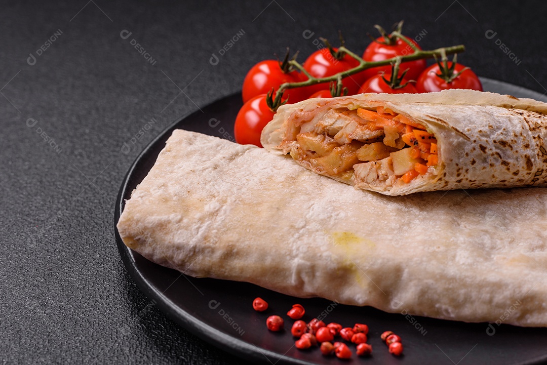 Delicioso rolo suculento ou shawarma com frango, tomate, salada e molho sobre um fundo escuro de concreto