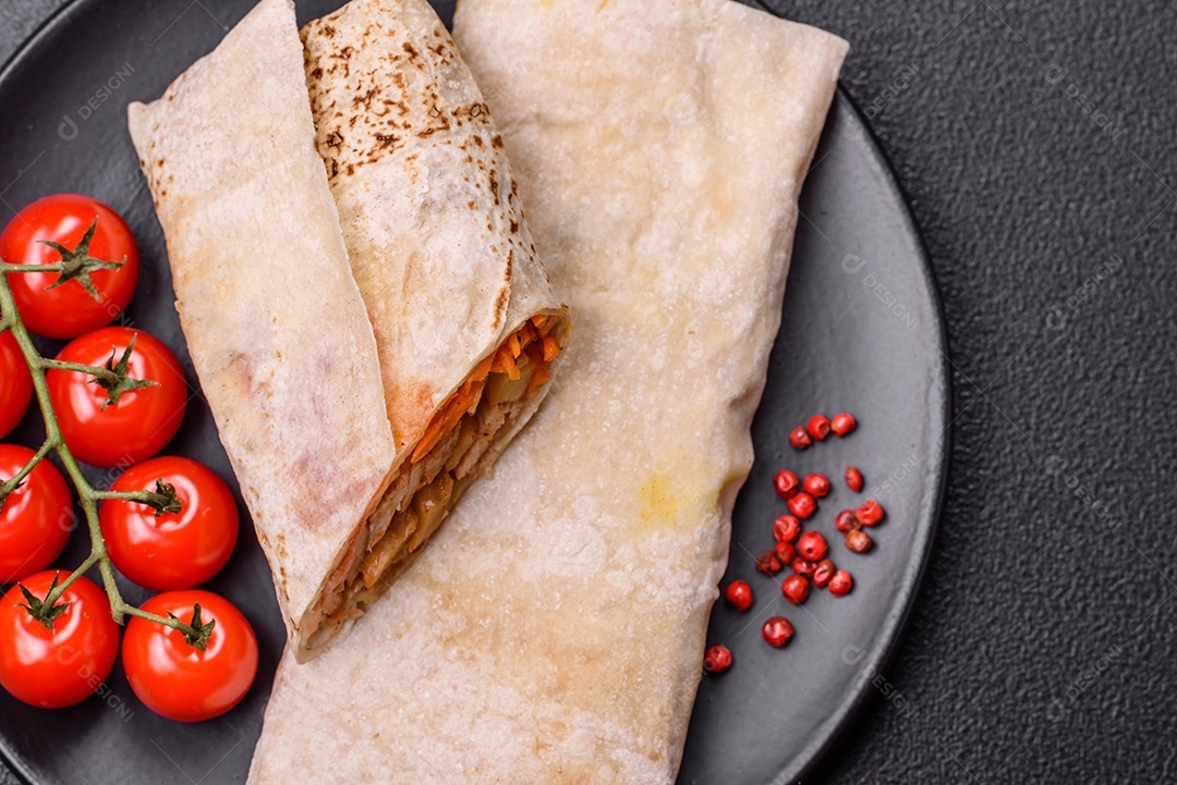 Delicioso rolo suculento ou shawarma com frango, tomate, salada e molho sobre um fundo escuro de concreto