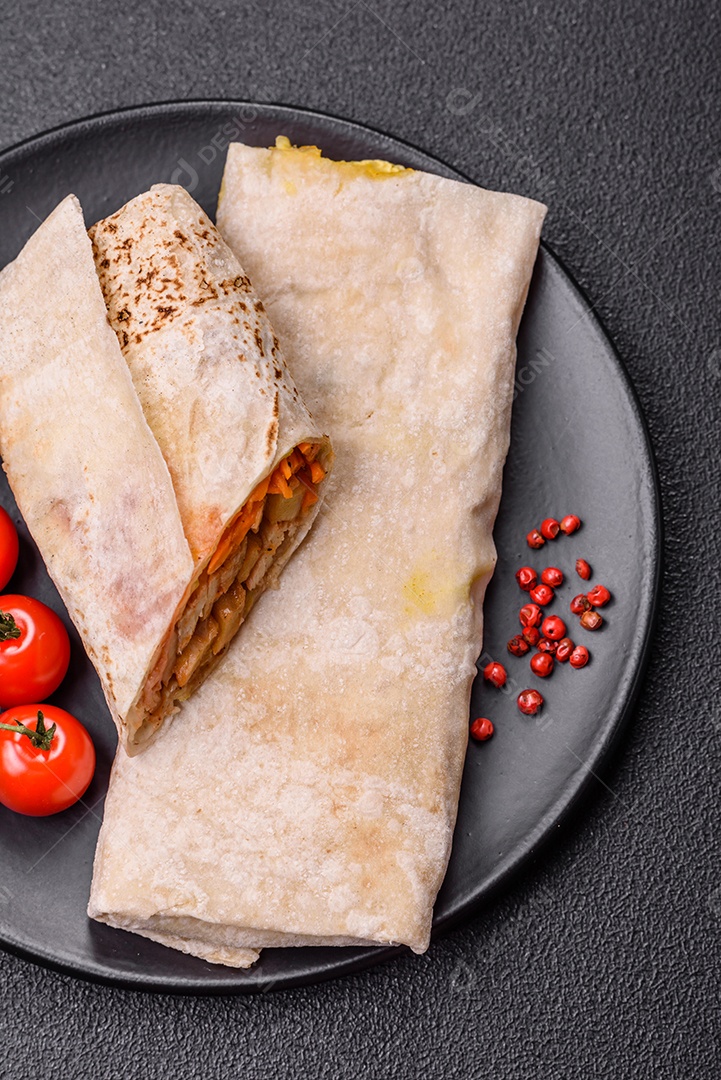 Delicioso rolo suculento ou shawarma com frango, tomate, salada e molho sobre um fundo escuro de concreto