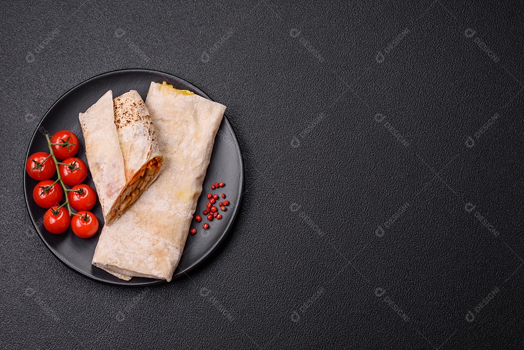 Delicioso rolo suculento ou shawarma com frango, tomate, salada e molho sobre um fundo escuro de concreto