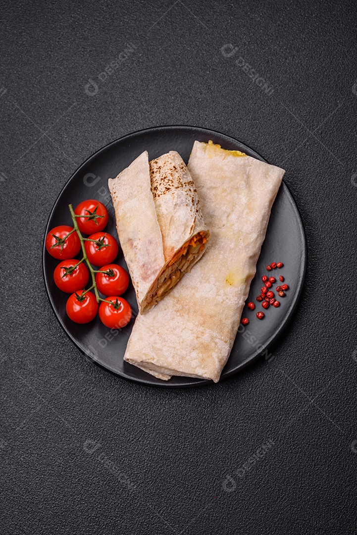 Delicioso rolo suculento ou shawarma com frango, tomate, salada e molho sobre um fundo escuro de concreto