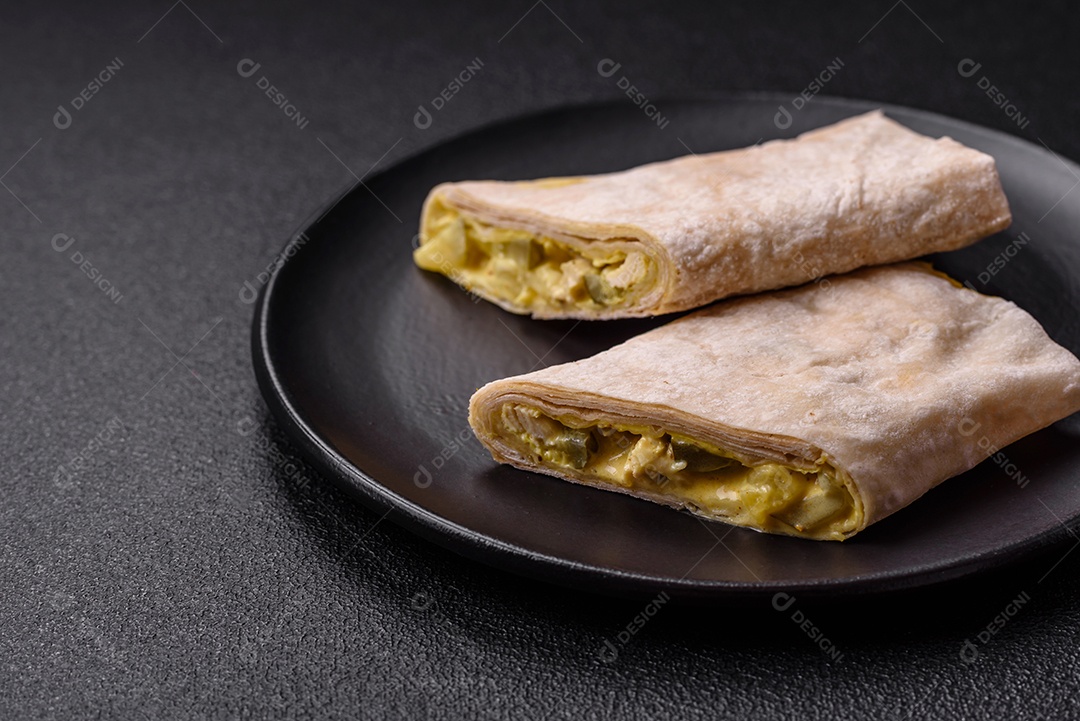 Delicioso rolo suculento ou shawarma com frango, tomate, salada e molho sobre um fundo escuro de concreto