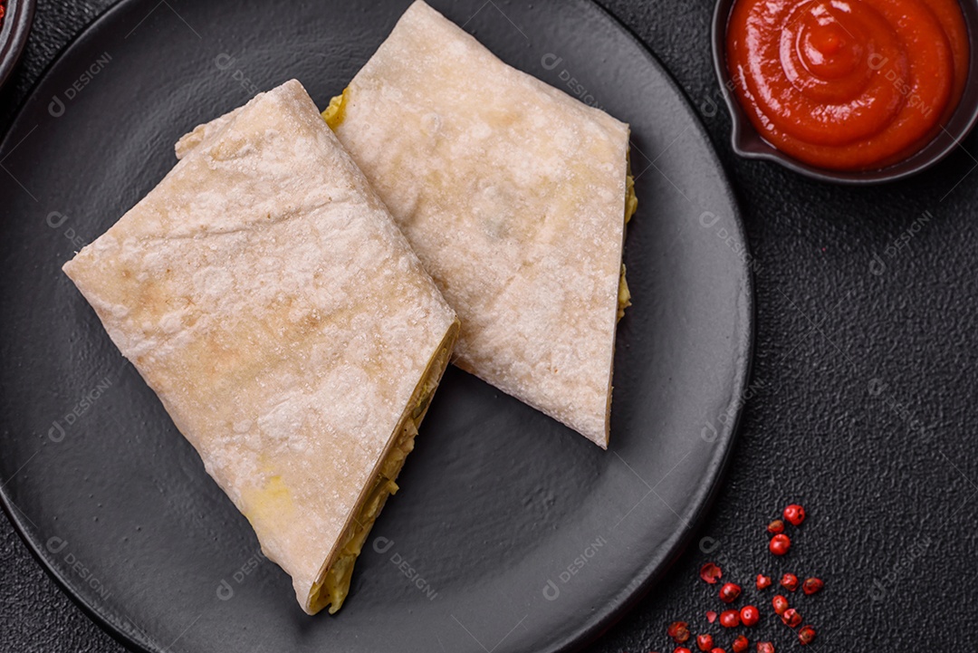 Delicioso rolo suculento ou shawarma com frango, tomate, salada e molho sobre um fundo escuro de concreto