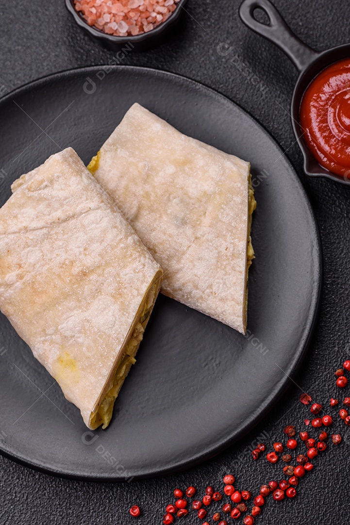 Delicioso rolo suculento ou shawarma com frango, tomate, salada e molho sobre um fundo escuro de concreto