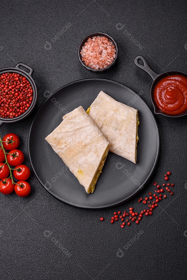 Delicioso rolo suculento ou shawarma com frango, tomate, salada e molho sobre um fundo escuro de concreto