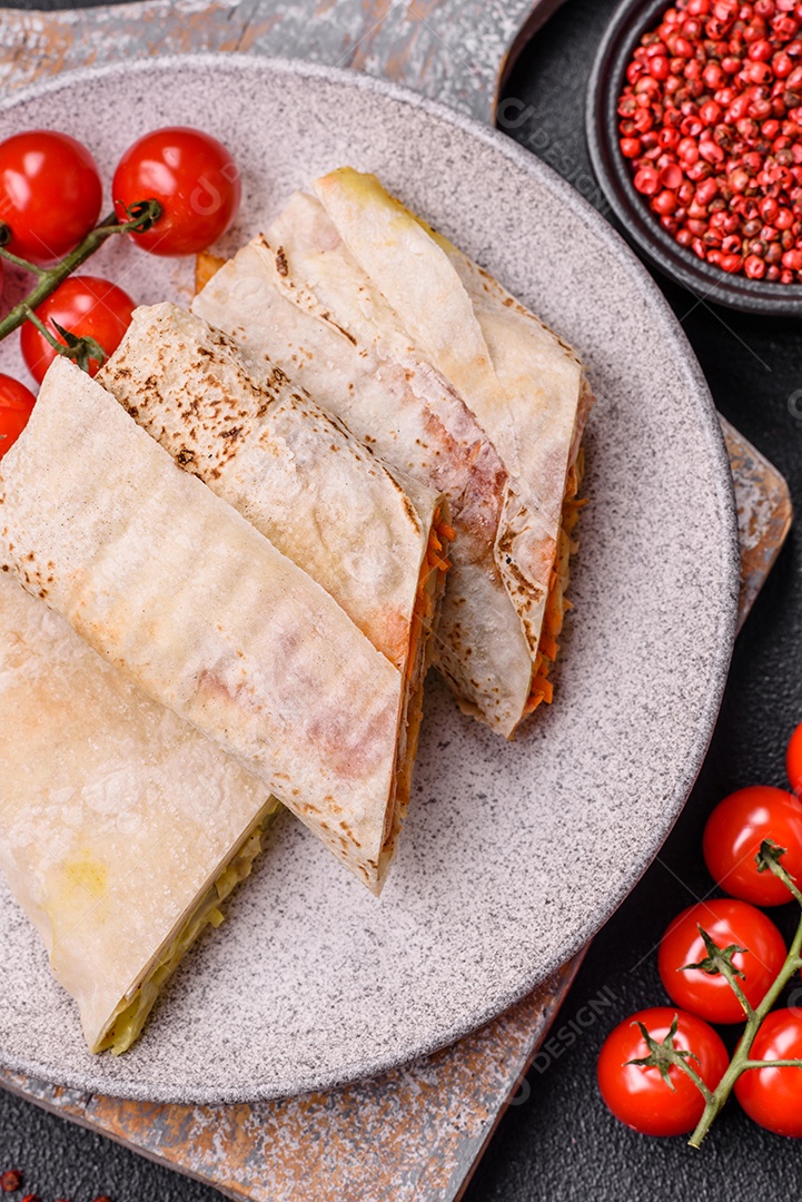 Delicioso rolo suculento ou shawarma com frango, tomate, salada e molho sobre um fundo escuro de concreto